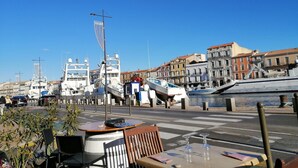 Um restaurante à beira-mar com mesas ao ar livre, com vista para uma marina com barcos e edifícios históricos.