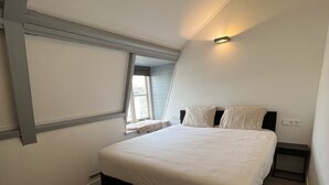 Una camera da letto con un letto, un comodino, una finestra e un soffitto spiovente.