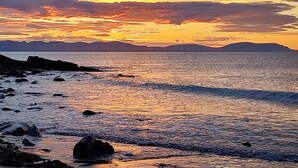 Solnedgang over en klippefyldt kystlinje med roligt vand, der spejler himlen.