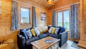 Et hyggeligt interiør i en hytte med en mørkegrå sofa, mønstrede gardiner og et træbord.