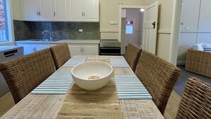 Une cuisine compacte avec des meubles blancs, un four encastré et un coin repas agrémenté d’un grand saladier posé sur la table.