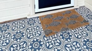 Une porte blanche fermée, dotée d’un panneau en verre dépoli, un paillasson orné d’un motif de poisson et un sol carrelé à motifs.