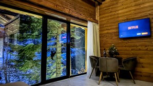 A modern interior with a large window, wooden walls, a flat-screen TV, and a dining area. - Jasna Boutique Chalet (Demanovska Dolina)
