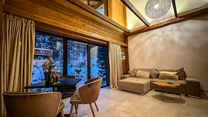 A modern living room with a wooden ceiling, a large window with a view of a snowy forest, a sofa, two armchairs, and a small table. - Jasna Boutique Chalet (Demanovska Dolina)
