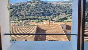 Une fenêtre donnant sur un paysage montagneux, avec un toit recouvert de tuiles et un ciel dégagé.