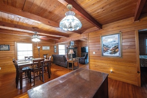 A wooden cabin interior with a dining area, a sofa, a fireplace, and a poster on the wall. - Perfect Family Friendly Cabin w/ privacy/arcade games/yard space in Townsend, TN (Townsend)