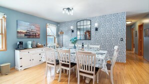 A dining area with a table set for four, white chairs, a white cabinet, and a painting on the wall.