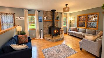 A cozy living room with a stone fireplace, a blue sofa, a grey sofa, and a patterned rug.