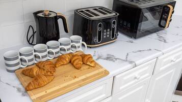 A kitchen counter with a toaster, a coffee maker, and a microwave. There are several mugs and croissants on the counter.