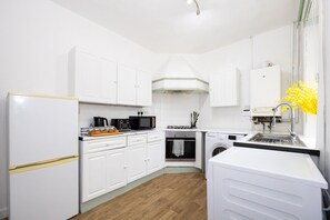 A compact kitchen with white cabinets, a microwave, a stove, and a washing machine. - Cosy Four Bedroom Terrace Rishton (Rishton)