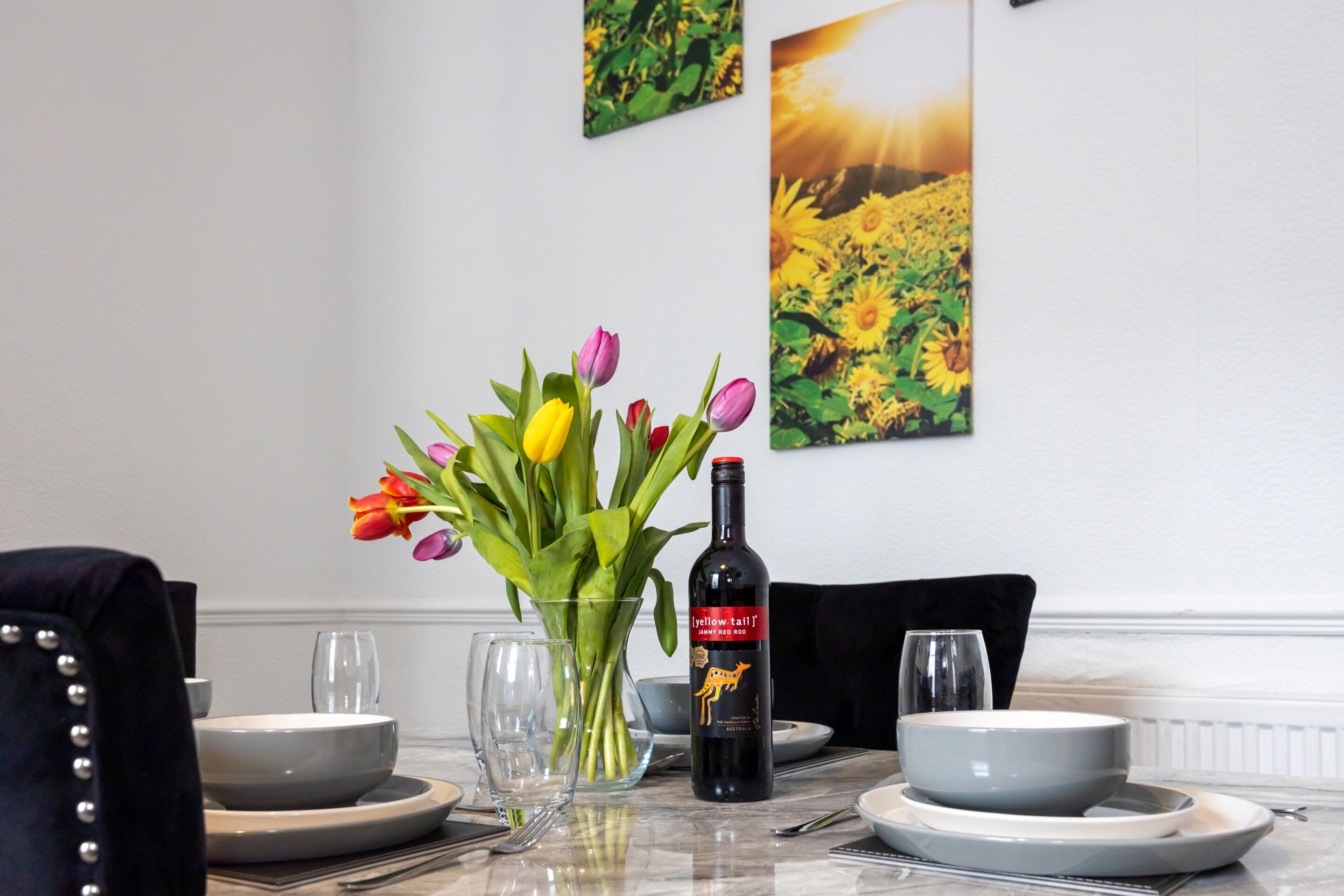 A dining table set with plates, bowls, a bottle of wine, and a vase of tulips.