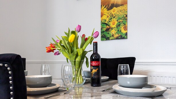 Een eettafel gedekt met borden, kommen, een fles wijn en een vaas tulpen.