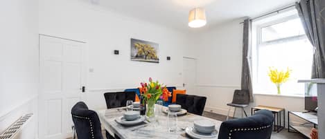 A dining area with a marble table, black upholstered chairs, a vase of flowers, and a painting on the wall.