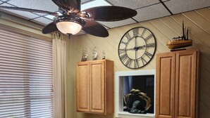 Una cocina con armarios de madera, una mesa de comedor, un ventilador de techo y un reloj de pared.