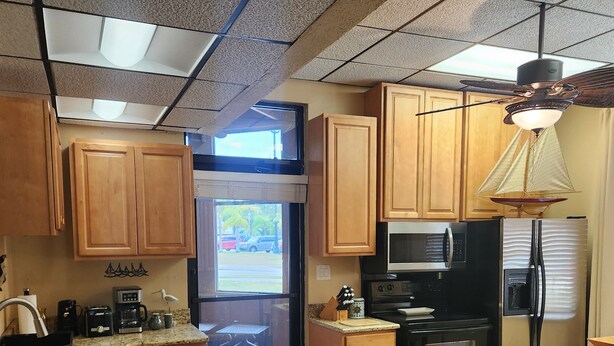 Una cocina con armarios de madera, un refrigerador negro, un microondas y un lavamanos.