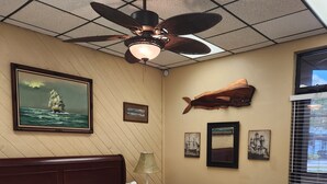 Un dormitorio con cama de madera, ventilador de techo y obras de arte en la pared, incluyendo una pintura de barco y fotografías enmarcadas.