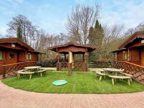 A wooden cabin with a gazebo, picnic tables, and a small pool.
