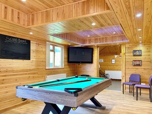 Una mesa de billar en una sala de madera con una pizarra que dice 'Marcador', un televisor y cuadros en las paredes.