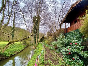 A garden with a narrow water channel, trees, and a wooden building. - Magnolia Lodge-UK46280 (Camerton, near Bath)
