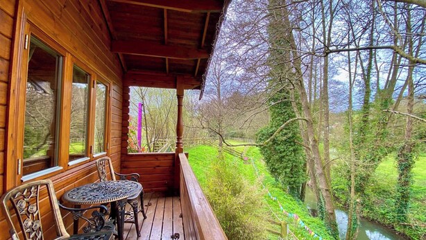 Een houten hutje met een balkon met uitzicht op een rivier en bos.