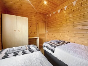 Una habitación de cabaña de madera con dos camas, un armario y un estante pequeño.
