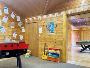 Una sala de madera con una mesa de billar, un dardo y una guitarra. Hay carteles en la pared y un póster de 'Toy Story'.
