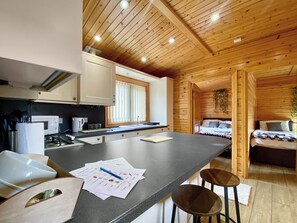 A kitchen with a central island, a dining area, and a bedroom with a bed and a hanging plant.