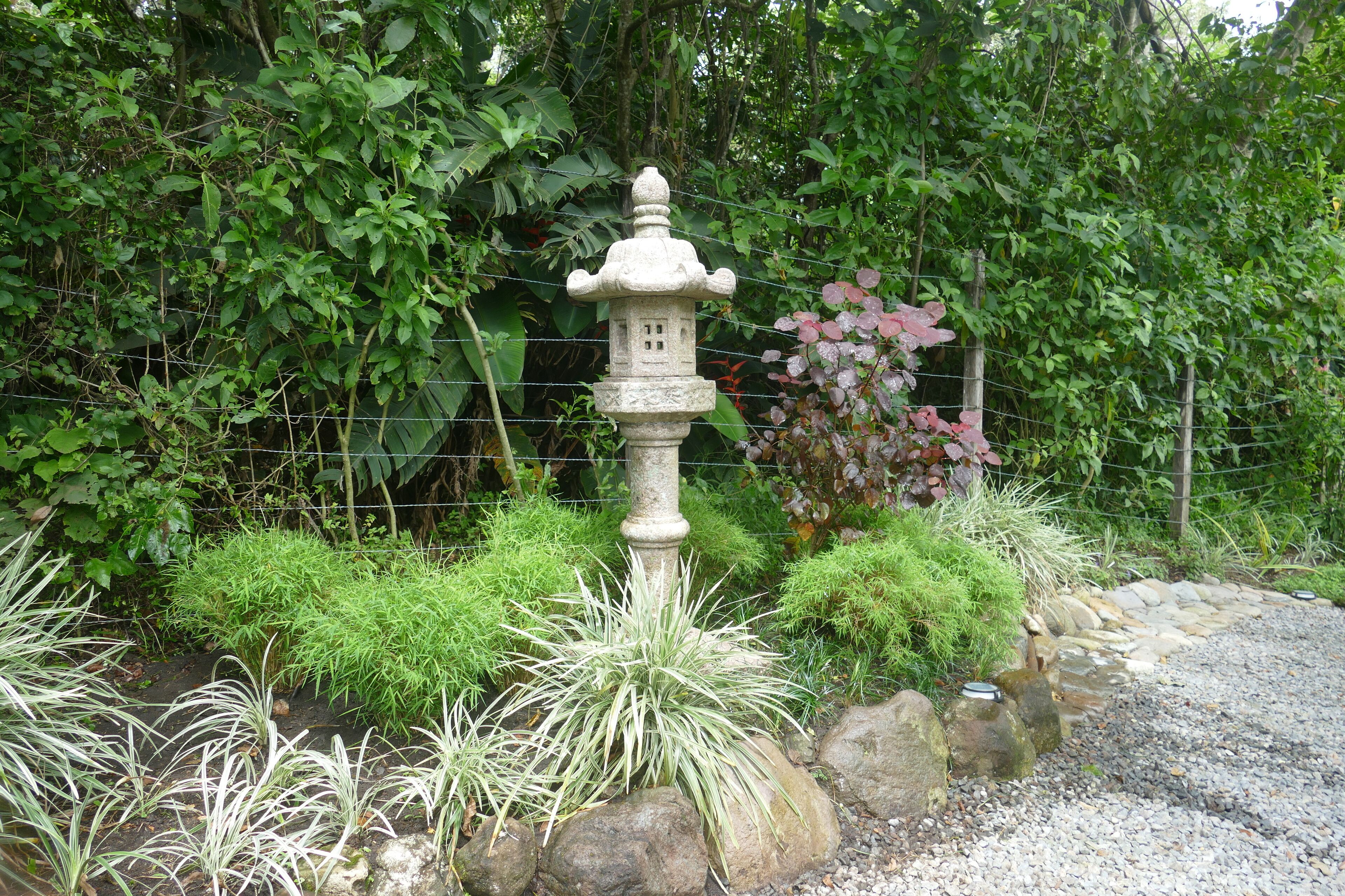 Un farol de piedra en un jardín con diversas plantas y un sendero de piedra.