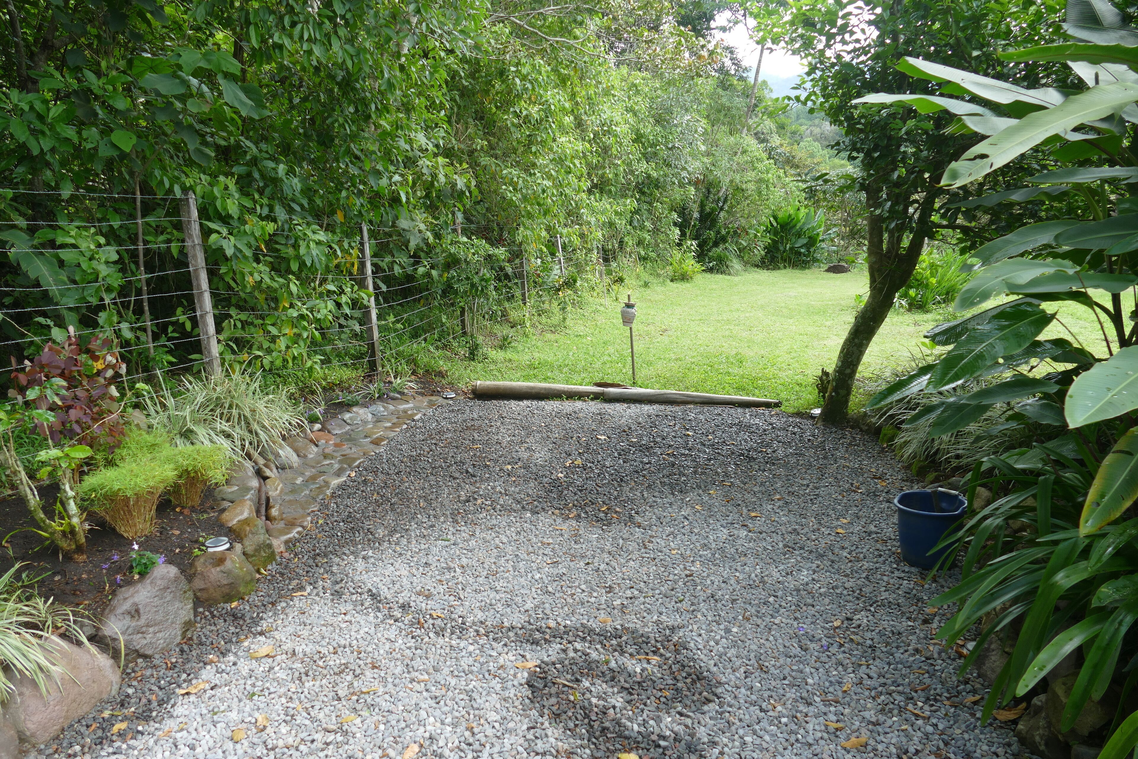A gravel pathway leading into a lush garden area with a wooden fence and a metal gate.