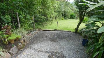 A gravel pathway leading into a lush garden area with a wooden fence and a metal gate.