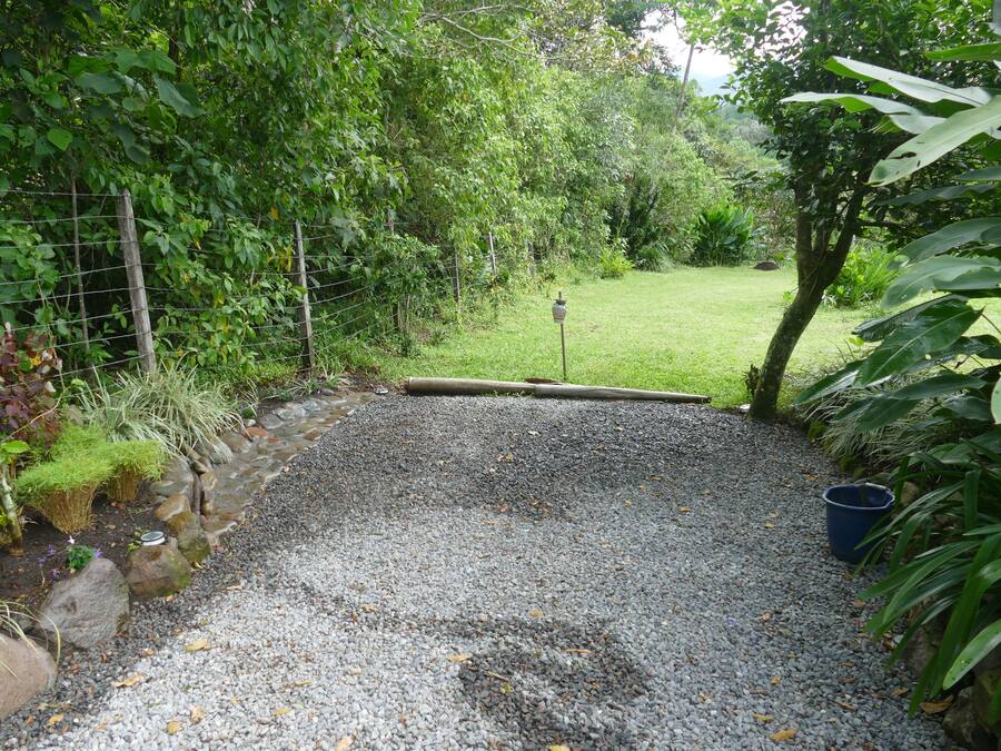 A gravel pathway leading into a lush garden area with a wooden fence and a metal gate.