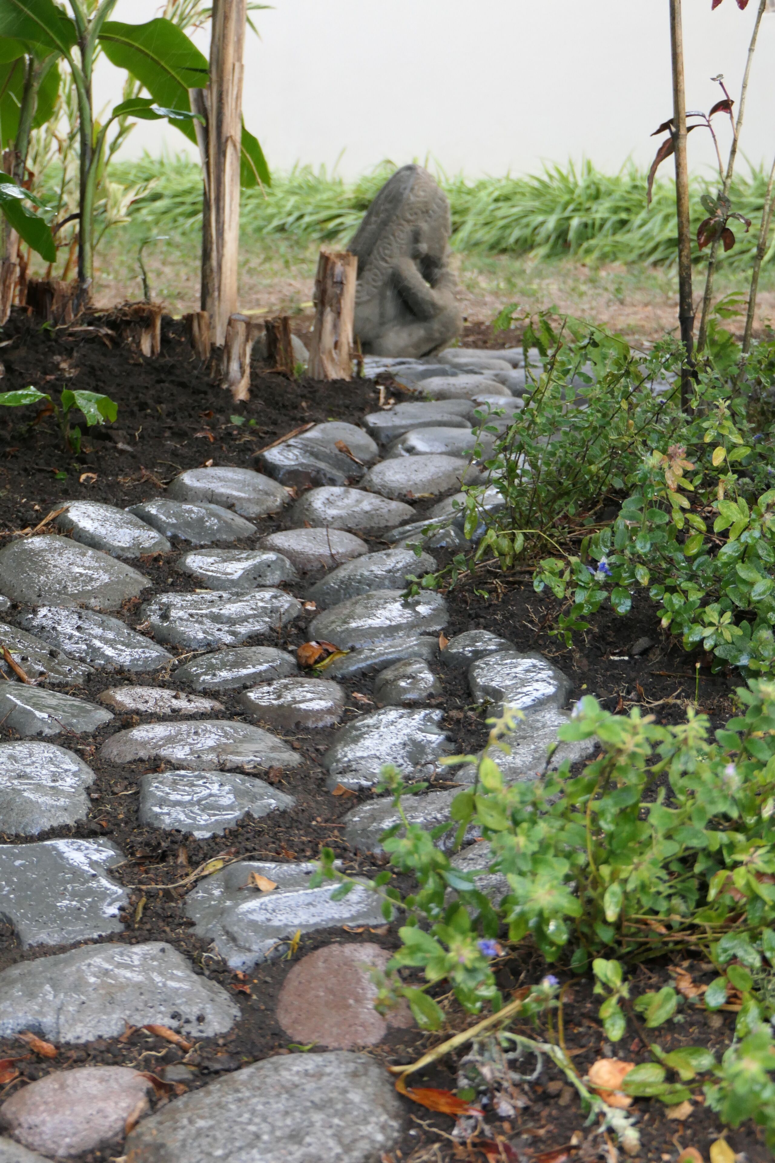 A stone pathway leading through a garden with a statue and various plants.