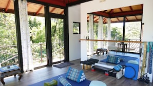 Una habitación amplia con un gran ventanal corredero que da a un balcón, una zona con tapete de yoga y una pequeña mesa de madera con un cuenco.