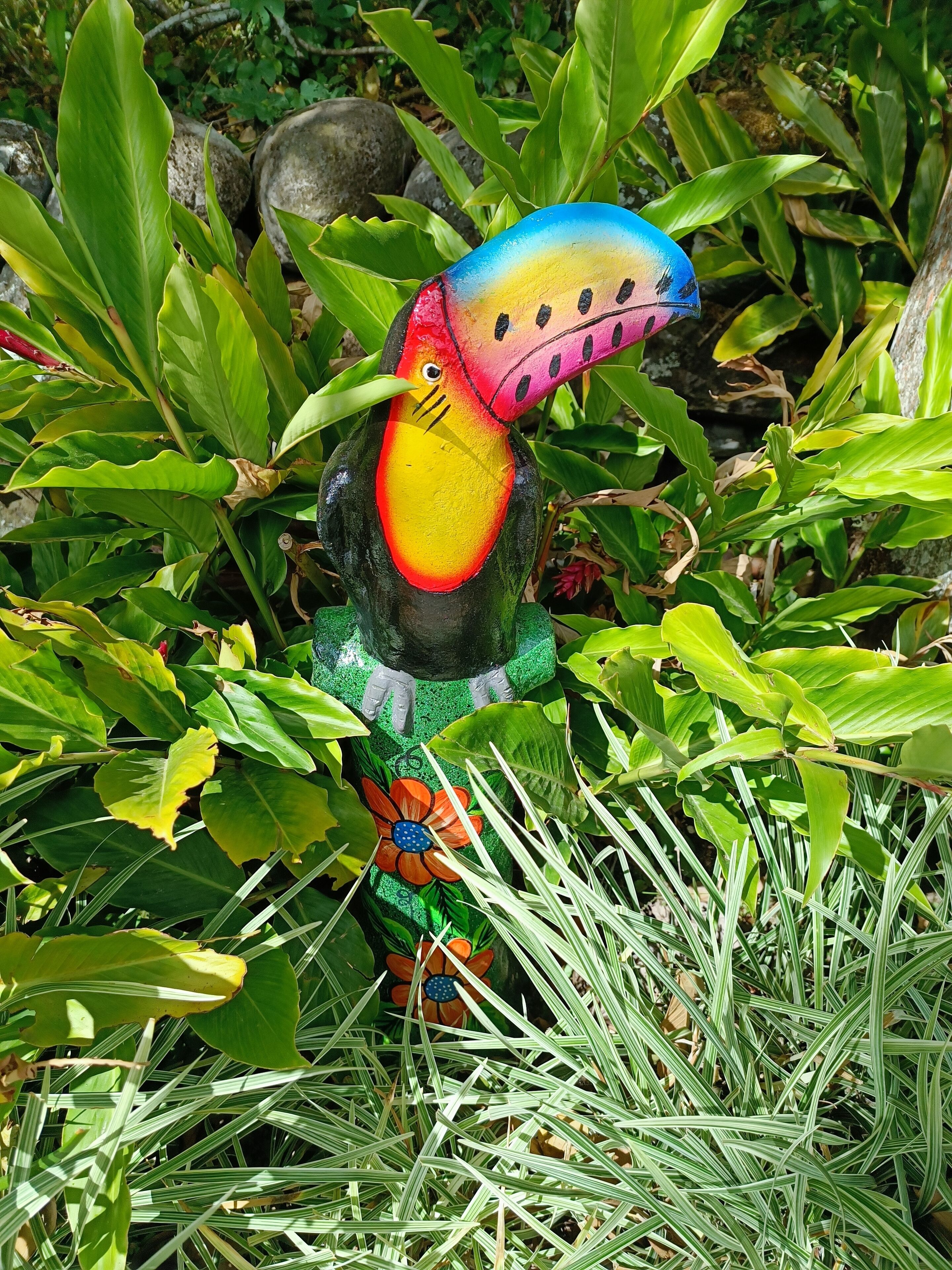 Una escultura de ave colorida en medio de un follaje verde exuberante.