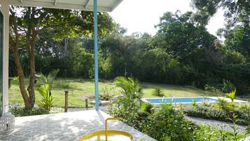 Un patio con una mesa amarilla y una mesa blanca, rodeado de exuberante follaje y una piscina.