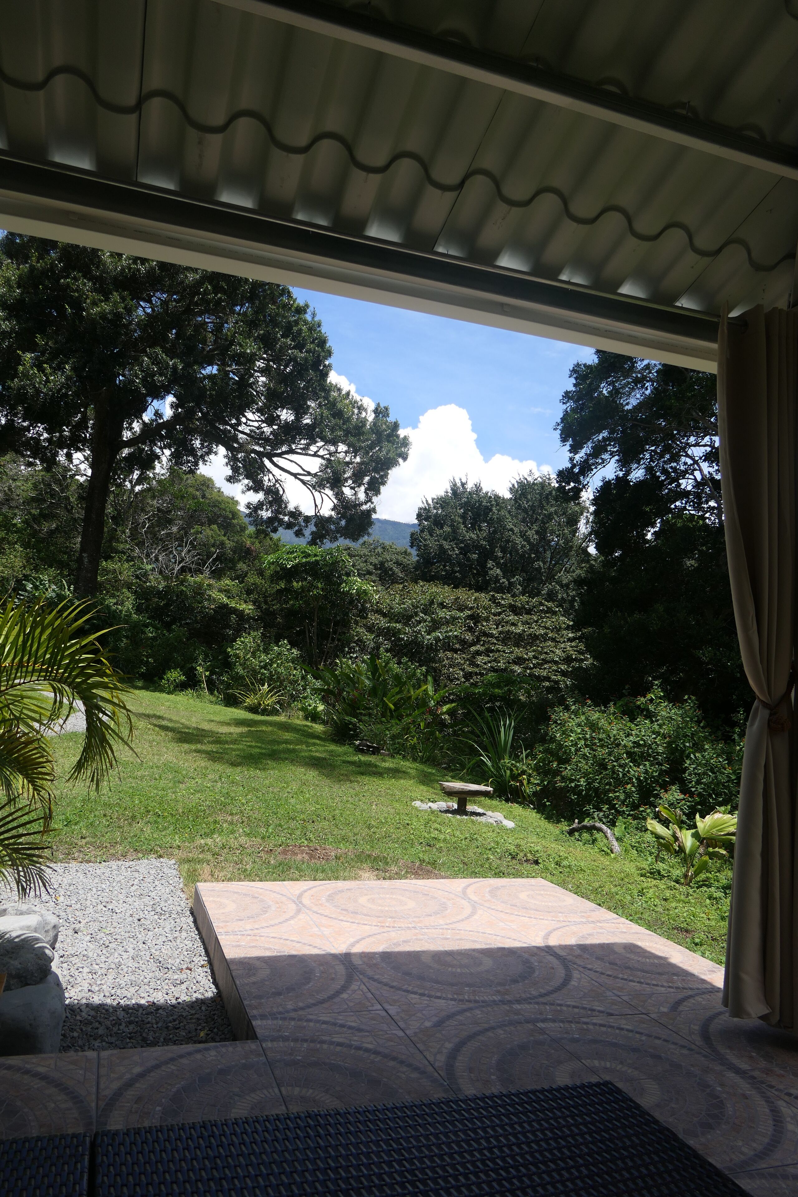 Un patio cubierto con vistas a un jardín exuberante y una montaña a lo lejos.