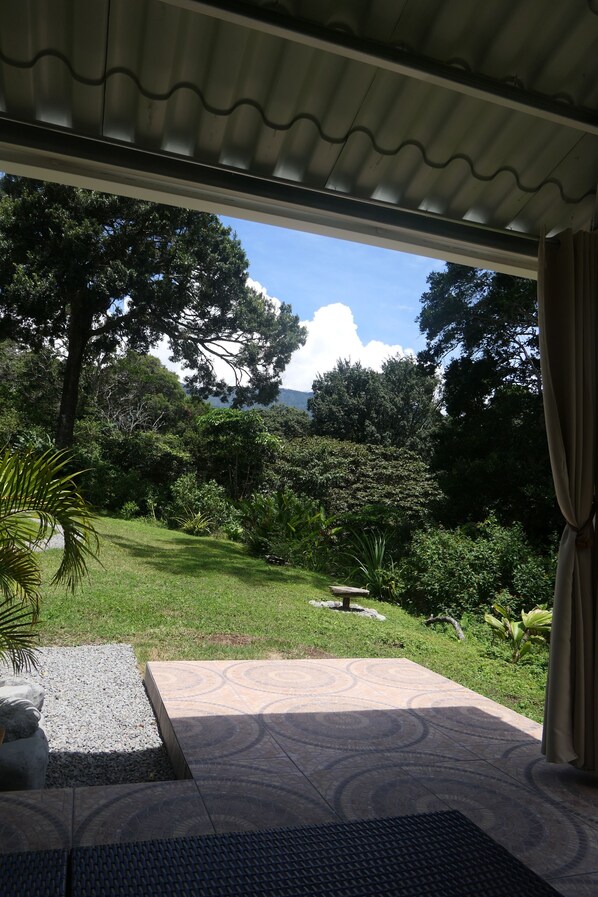 A covered patio with a view of a lush garden and a mountain in the distance.