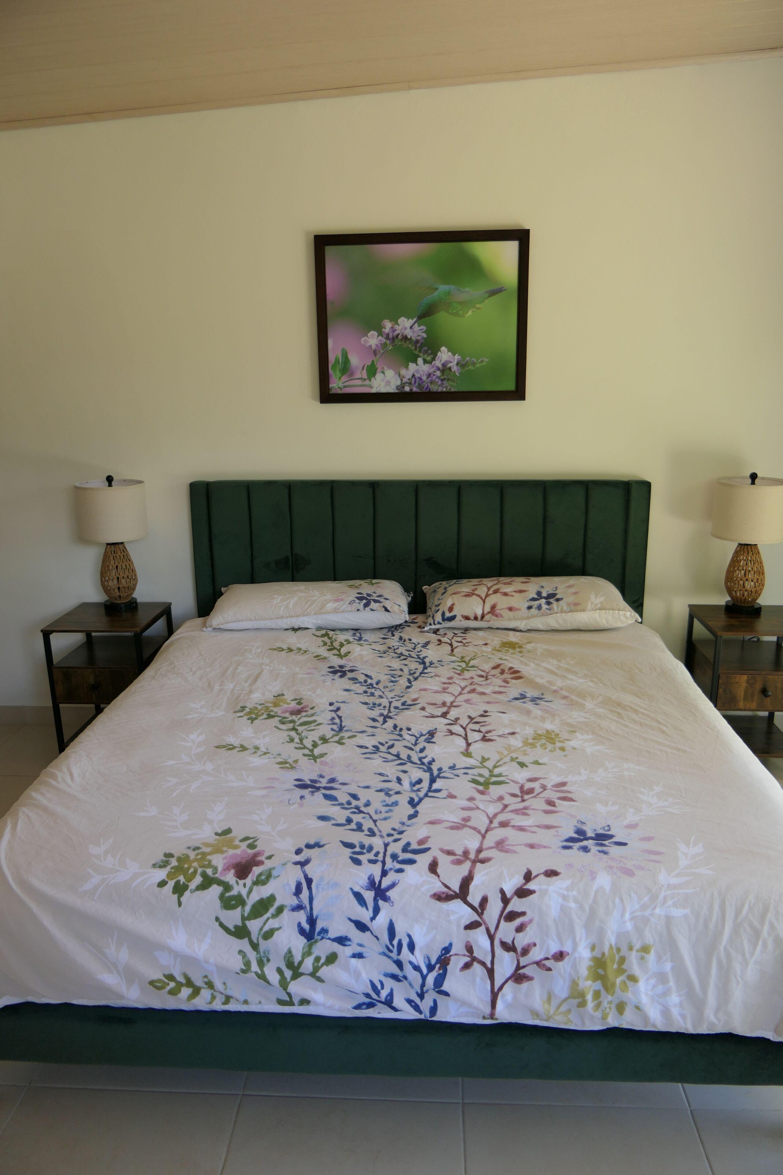 Un letto rifatto con una coperta a fiori, due comodini con lampade e un quadro incorniciato appeso al muro.