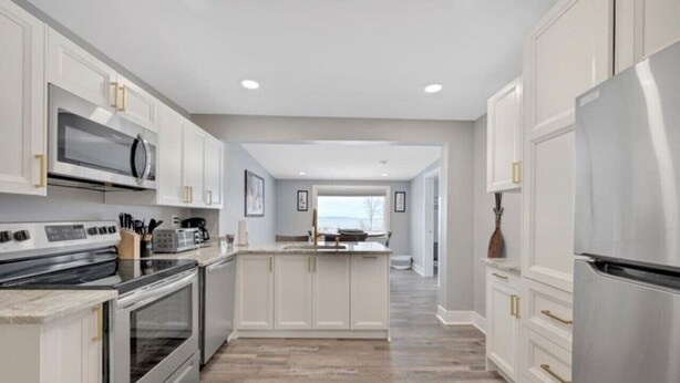 Una cocina moderna con muebles blancos, electrodomésticos de acero inoxidable y un suelo de madera en patrón de espiga.