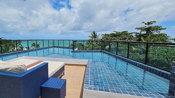 A rooftop infinity pool with blue-tiled edges, surrounded by wicker lounge chairs and a wooden deck. - Na Praia Flats Maraca 108 (Ipojuca)