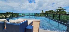 A rooftop infinity pool with blue-tiled edges, surrounded by wicker lounge chairs and a wooden deck. - Na Praia Flats Maraca 108 (Ipojuca)