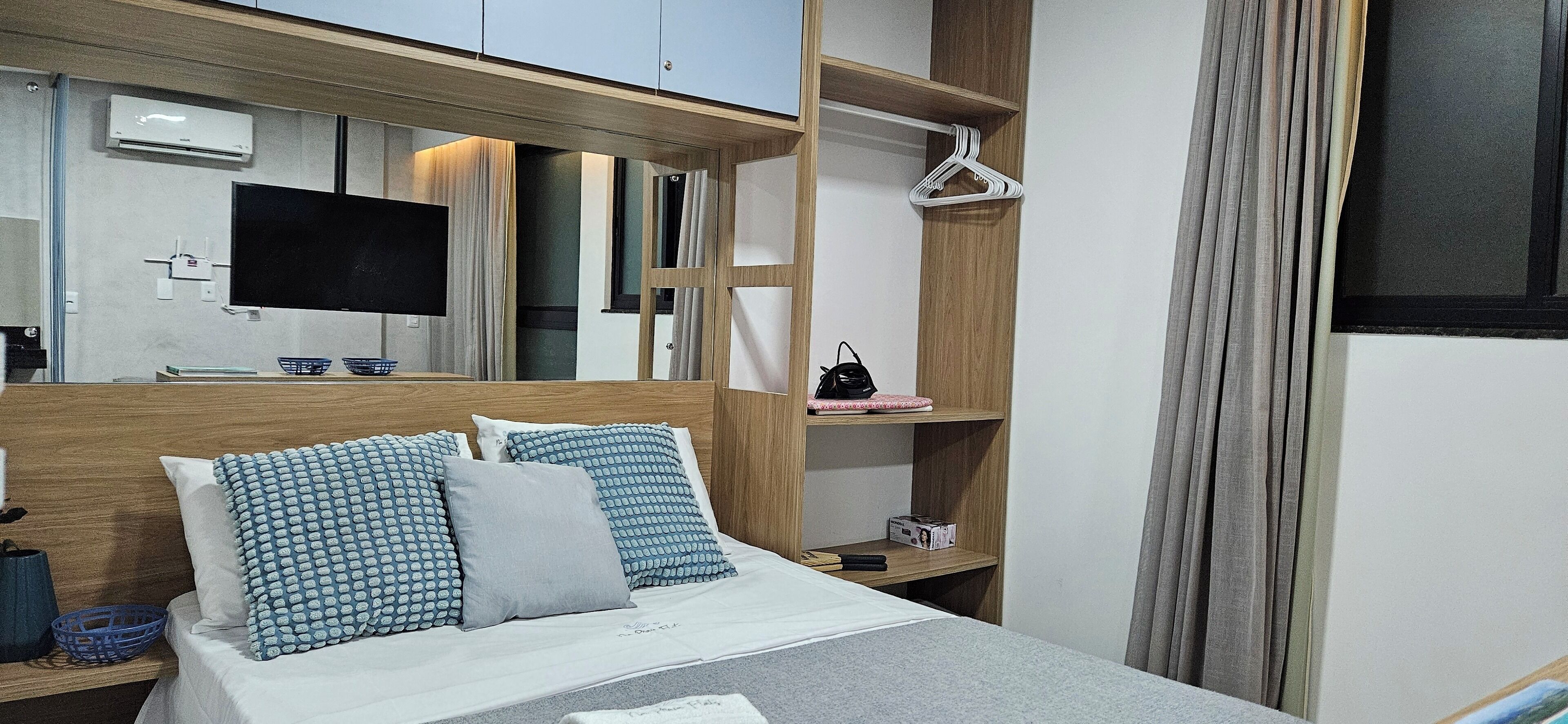 Una habitación de hotel moderna con cama, televisor, armario y espejo.