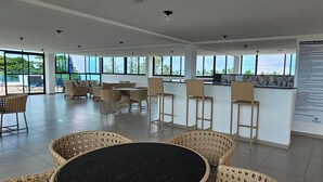 A spacious indoor area with wicker furniture, large windows, and a door with a sign. - Na Praia Flats Maraca 108 (Ipojuca)