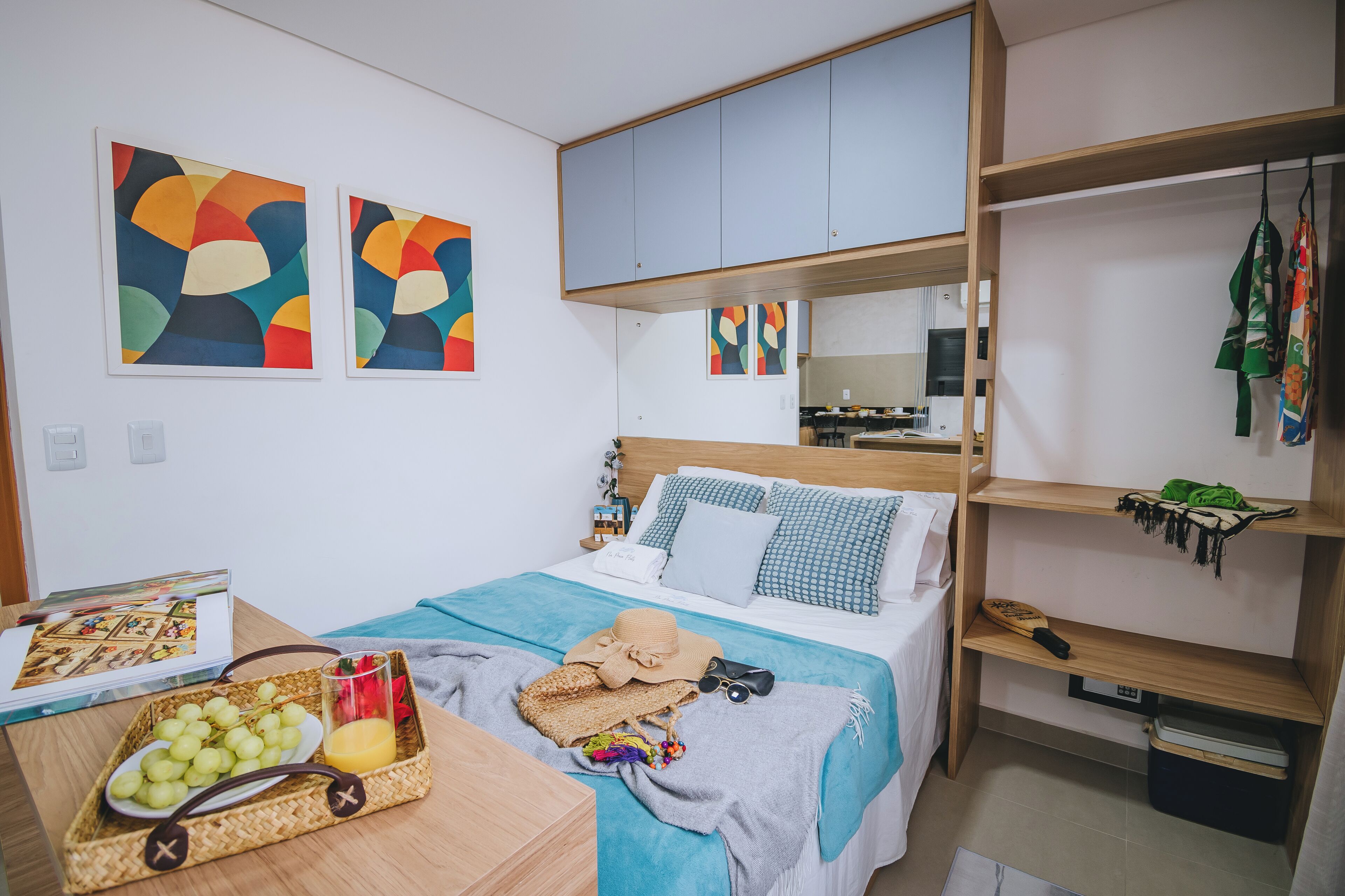 Une chambre à coucher avec un lit, une table de chevet sur laquelle se trouve un panier de fruits, un miroir et une œuvre d’art abstrait accrochée au mur.