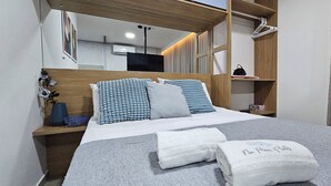 A neatly made bed with blue and white patterned pillows, a grey blanket, and two white towels with text. - Na Praia Flats Maraca 108 (Ipojuca)