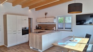 Une cuisine moderne avec des poutres en bois, des meubles blancs, un îlot central et un coin repas comprenant une table et des chaises.