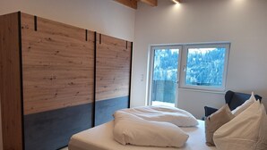 Une chambre à coucher avec un lit, des oreillers, une armoire et une fenêtre donnant sur des arbres couverts de neige.