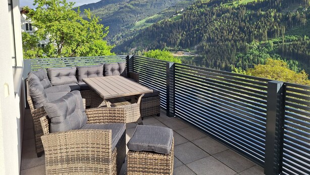 Un balcon doté de meubles en osier et offrant une vue sur un paysage montagneux.