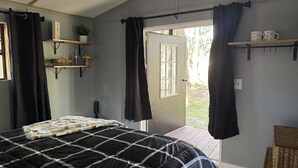 A bedroom with a bed, a window, a door, and a shelf with items. - RAINBOW RANCH CABINS (Dunnellon)