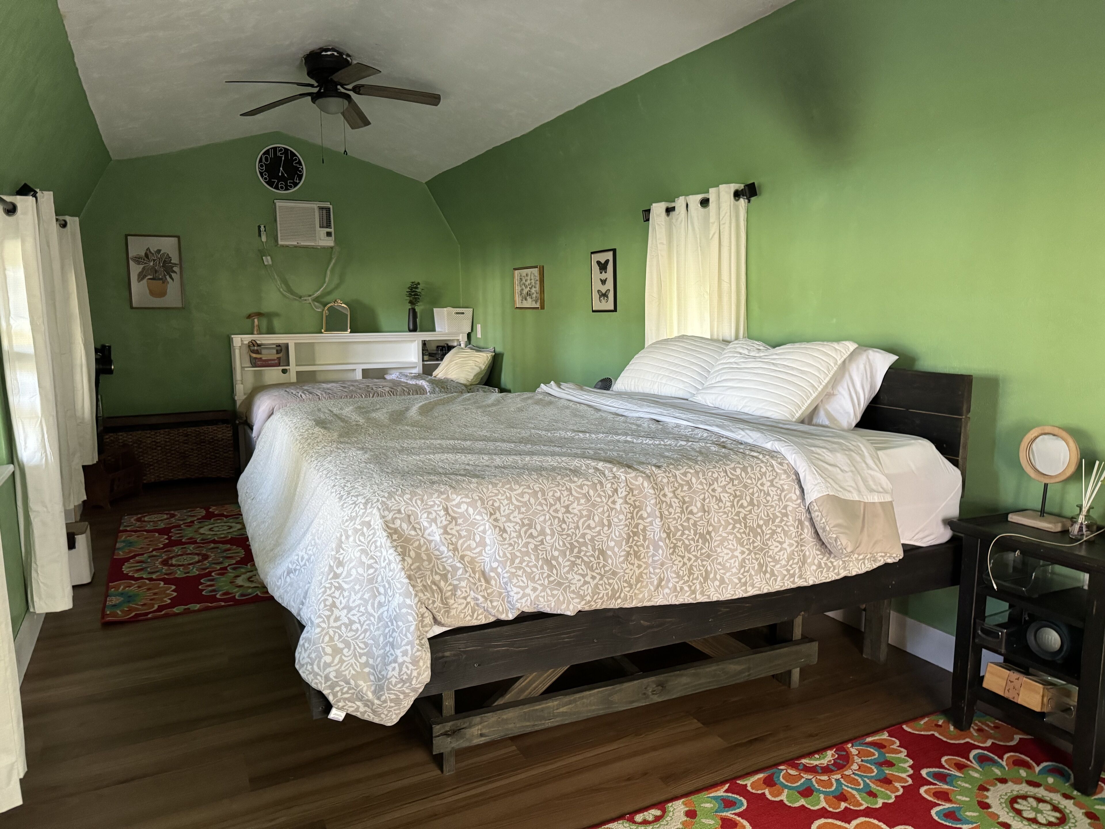 Un dormitorio con cama, ventilador de techo, reloj y mesita de noche con espejo.